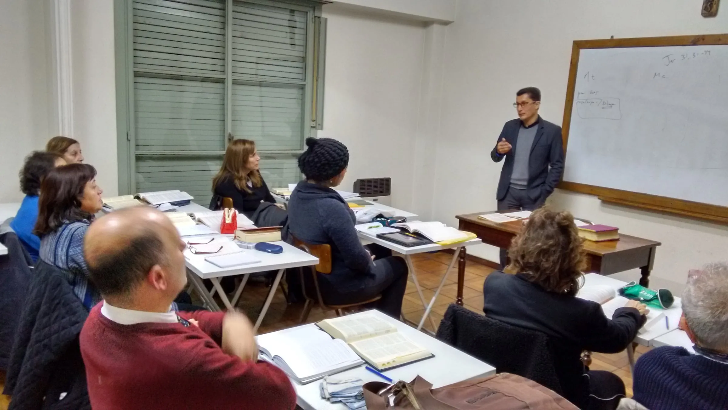 Clase en el Centro Bíblico: el profesor explica un texto frente al pizarrón mientras los alumnos siguen la lectura en sus biblias.